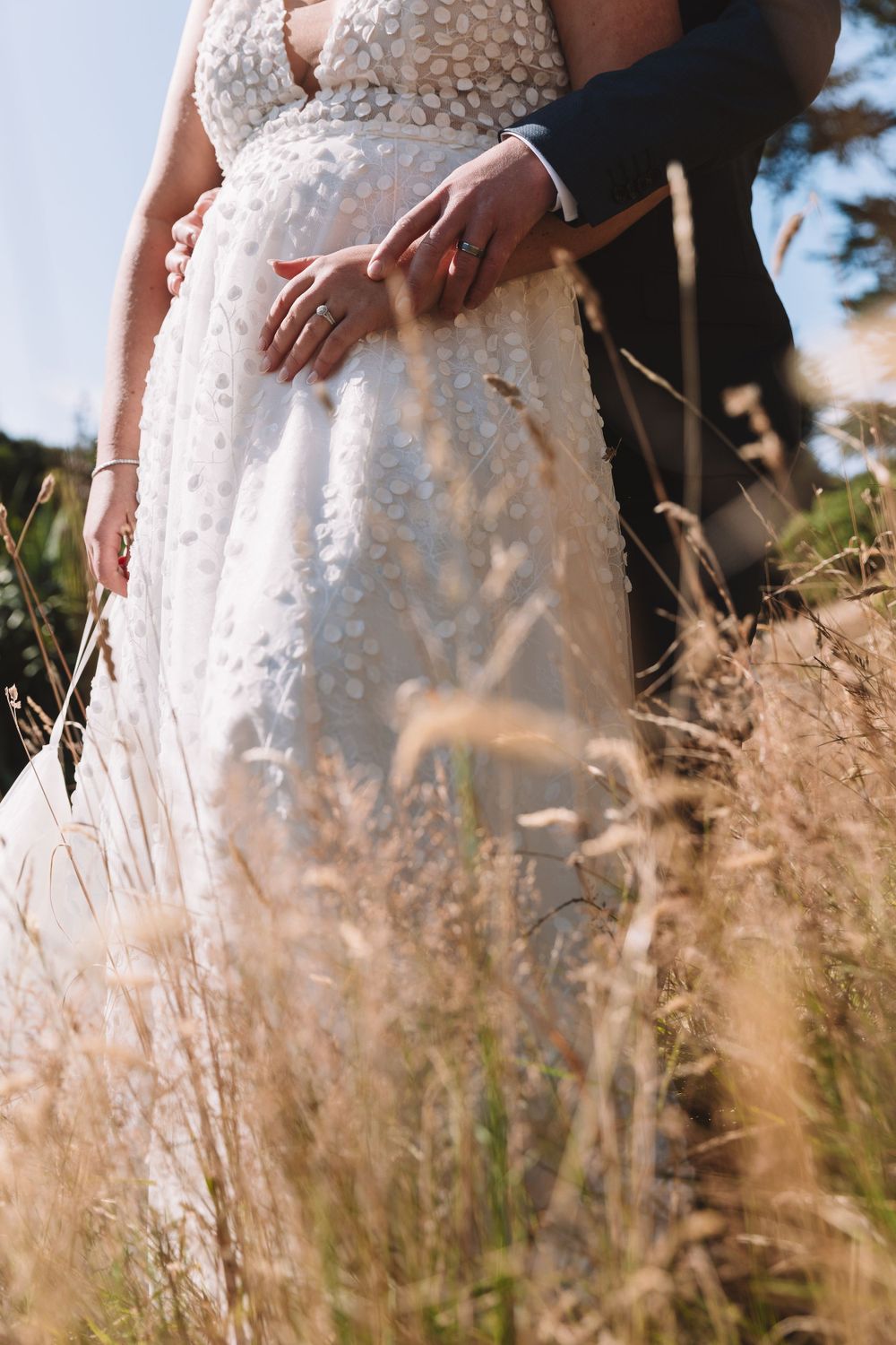 Close-up detail of a beaded white wedding dress amid tall golden grass.