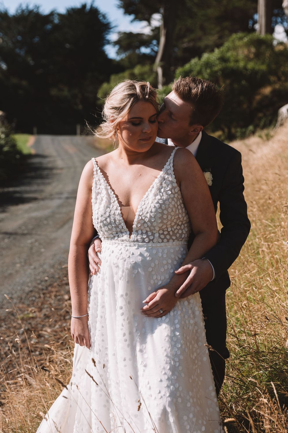 Intimate wedding moment captured on a rural road lined with trees.