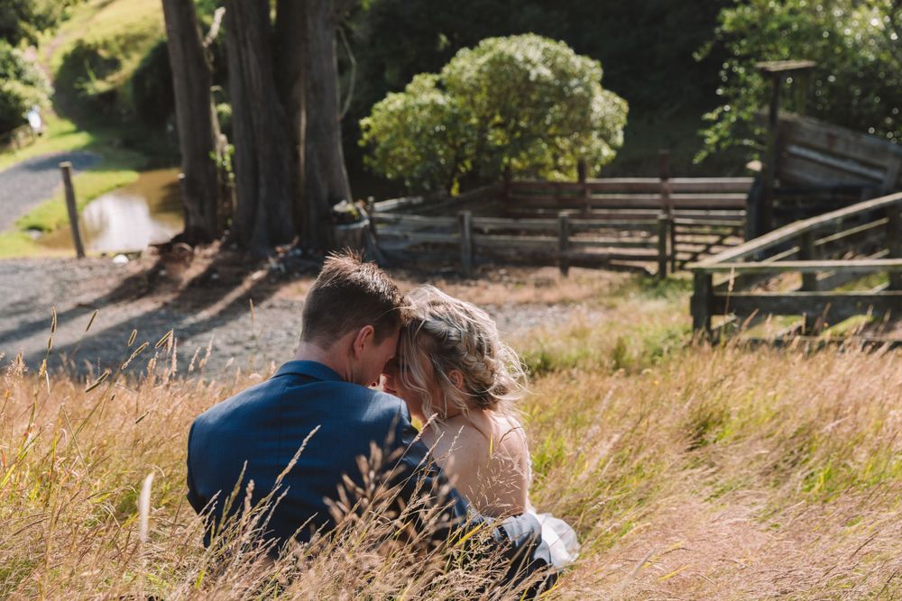 Romantic moment shared while sitting in tall grass with trees in background.