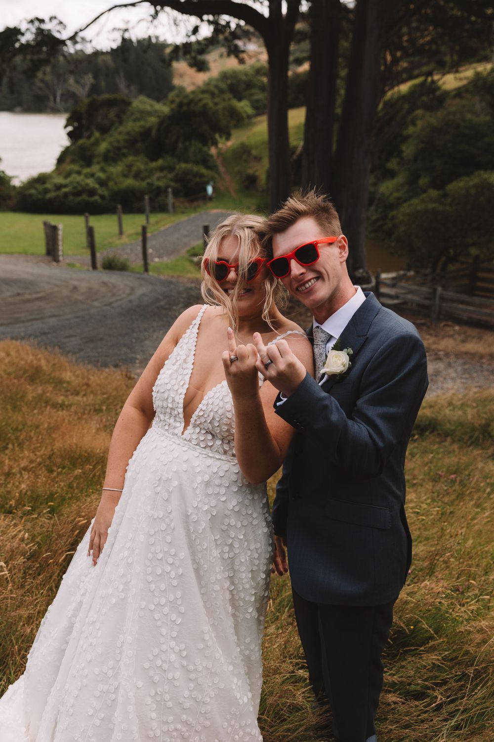 Fun wedding photo with couple wearing novelty sunglasses by a lake.
