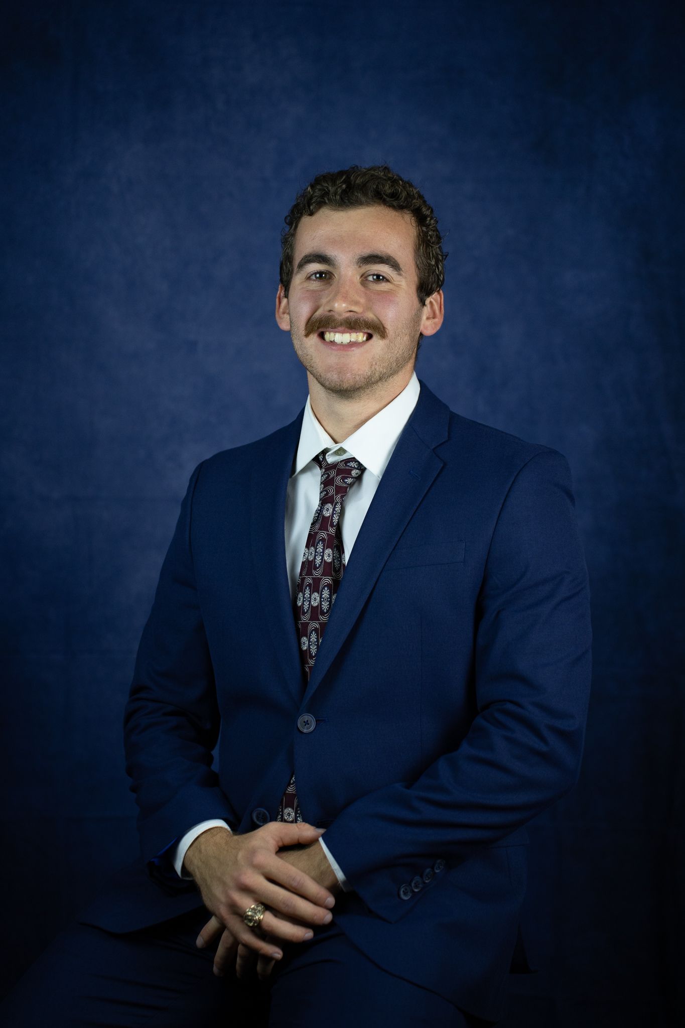 Professional portrait of someone in business attire with blue striped shirt and patterned tie.