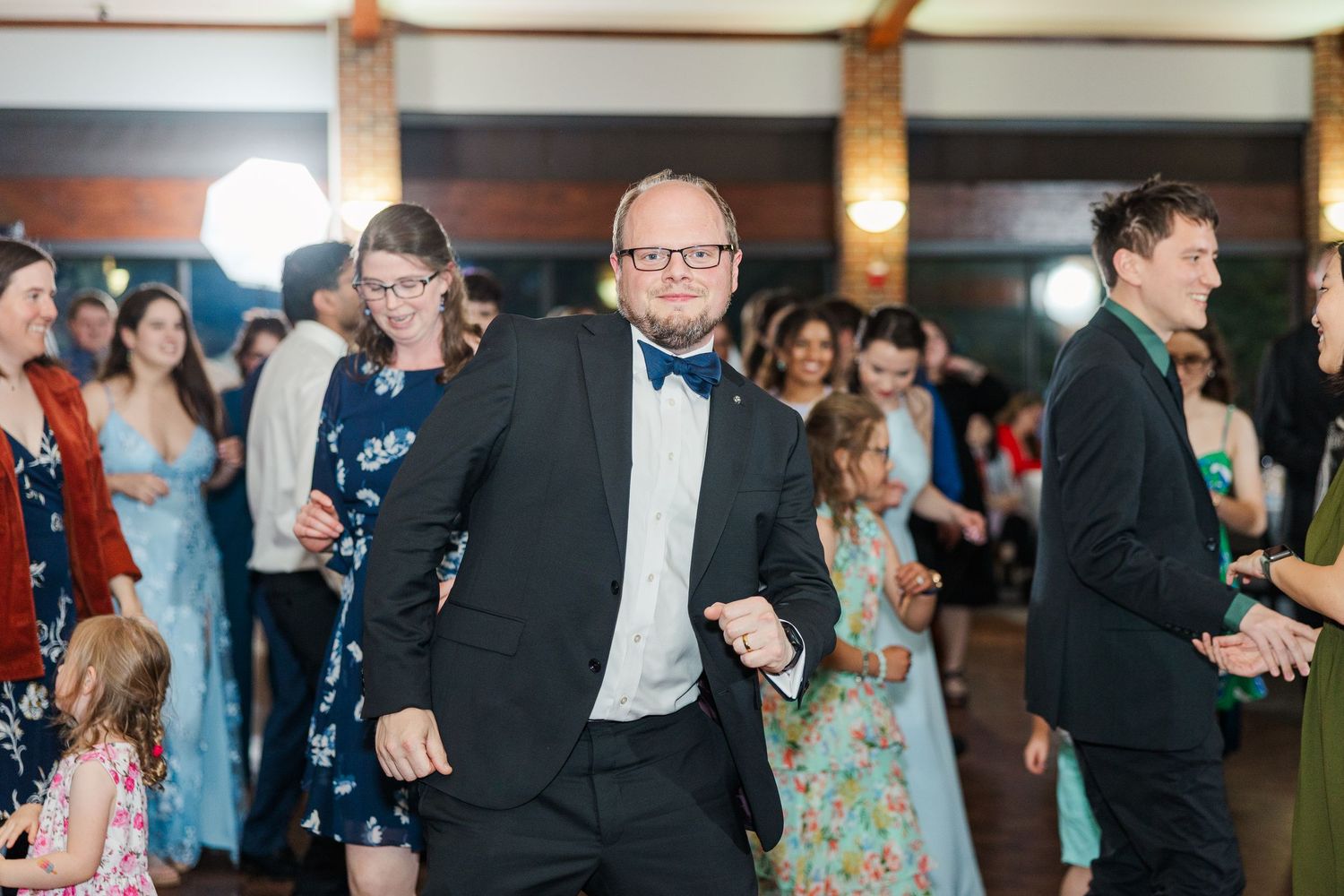 People dancing and enjoying a wedding reception in formal attire on a crowded dance floor.