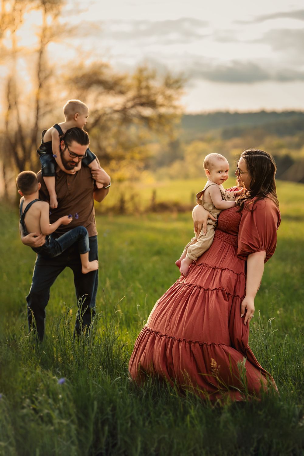 Family enjoying a sunset moment in a grassy field with warm golden light filtering through trees in the background.