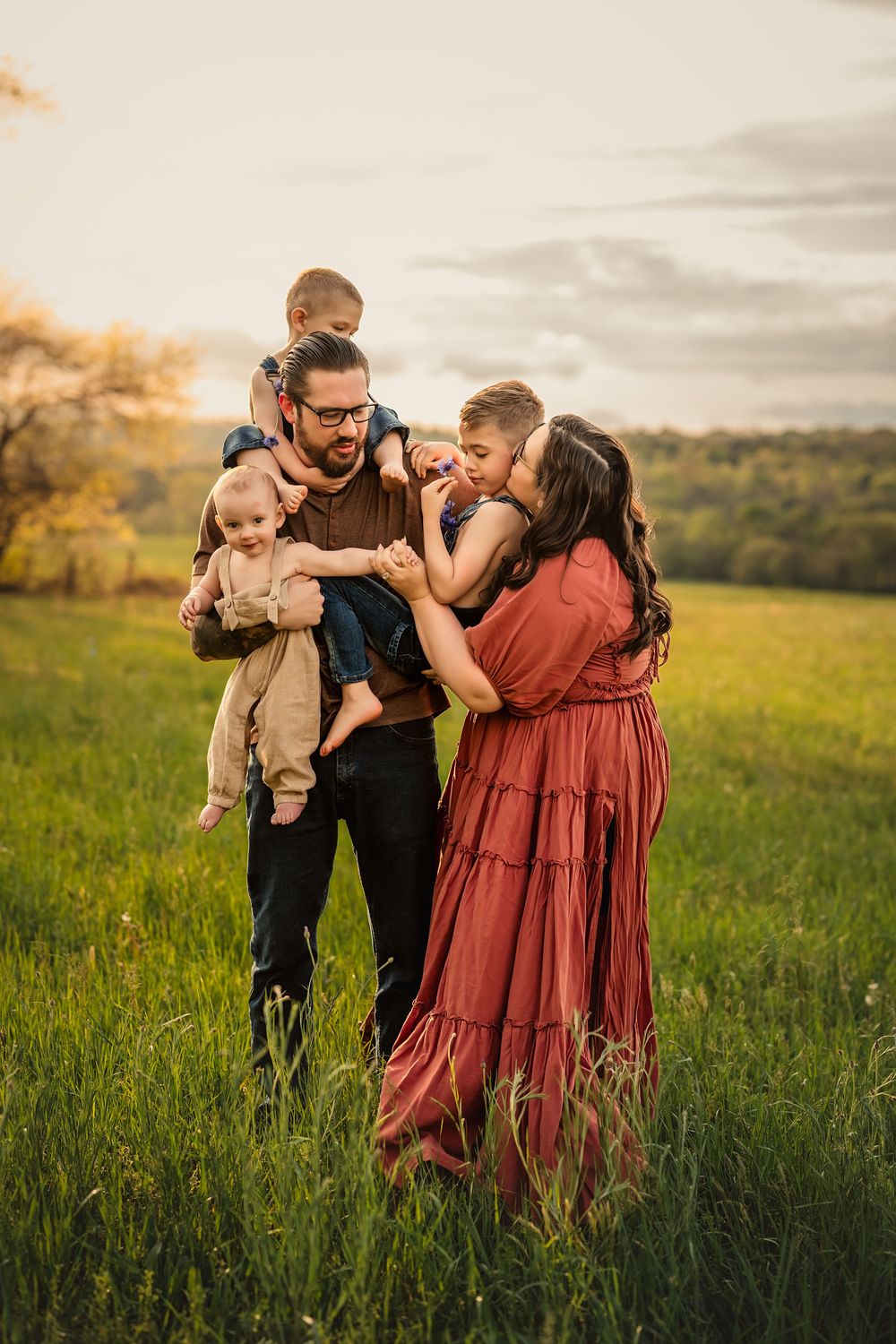 Family of five shares an intimate moment in a grassy field at sunset against a natural landscape.