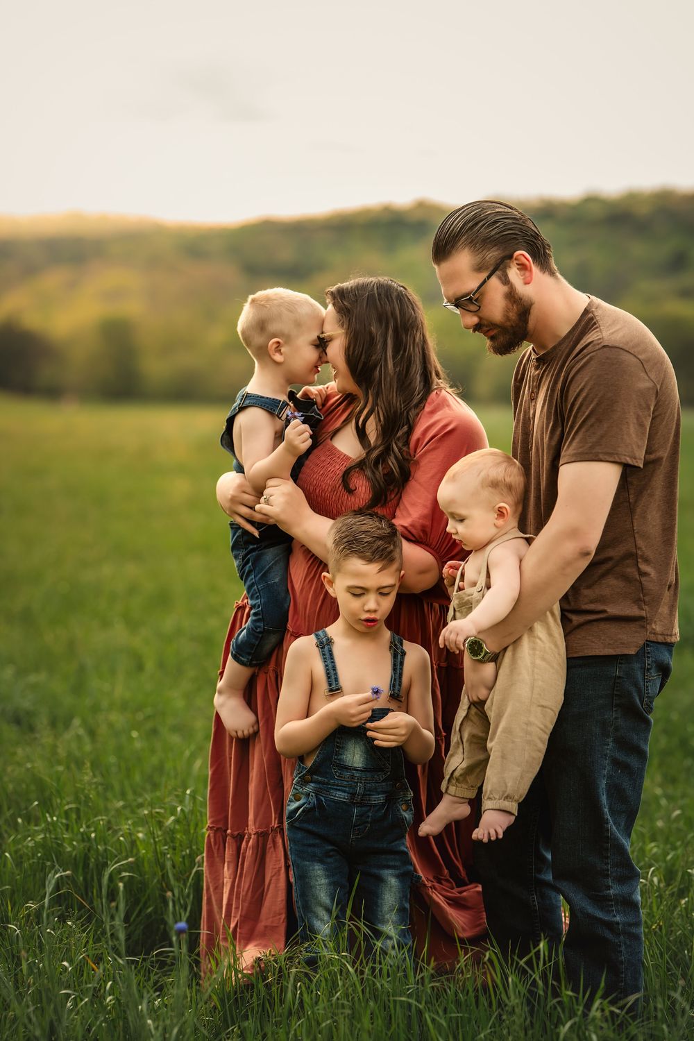 Family gathering in a field at golden hour for family photos among tall grass and rolling hills in the background.