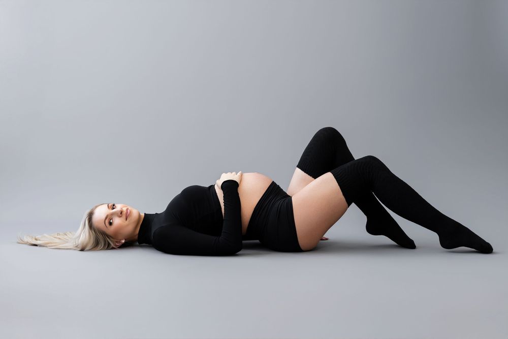 Artistic maternity photography with dramatic poses on grey backdrop.