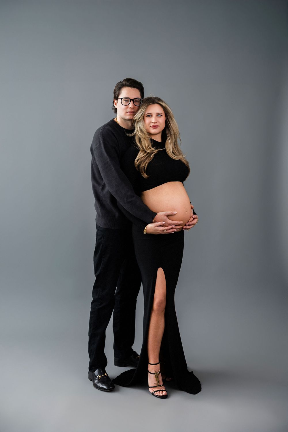 Sophisticated maternity portrait of couple in black attire against grey backdrop.