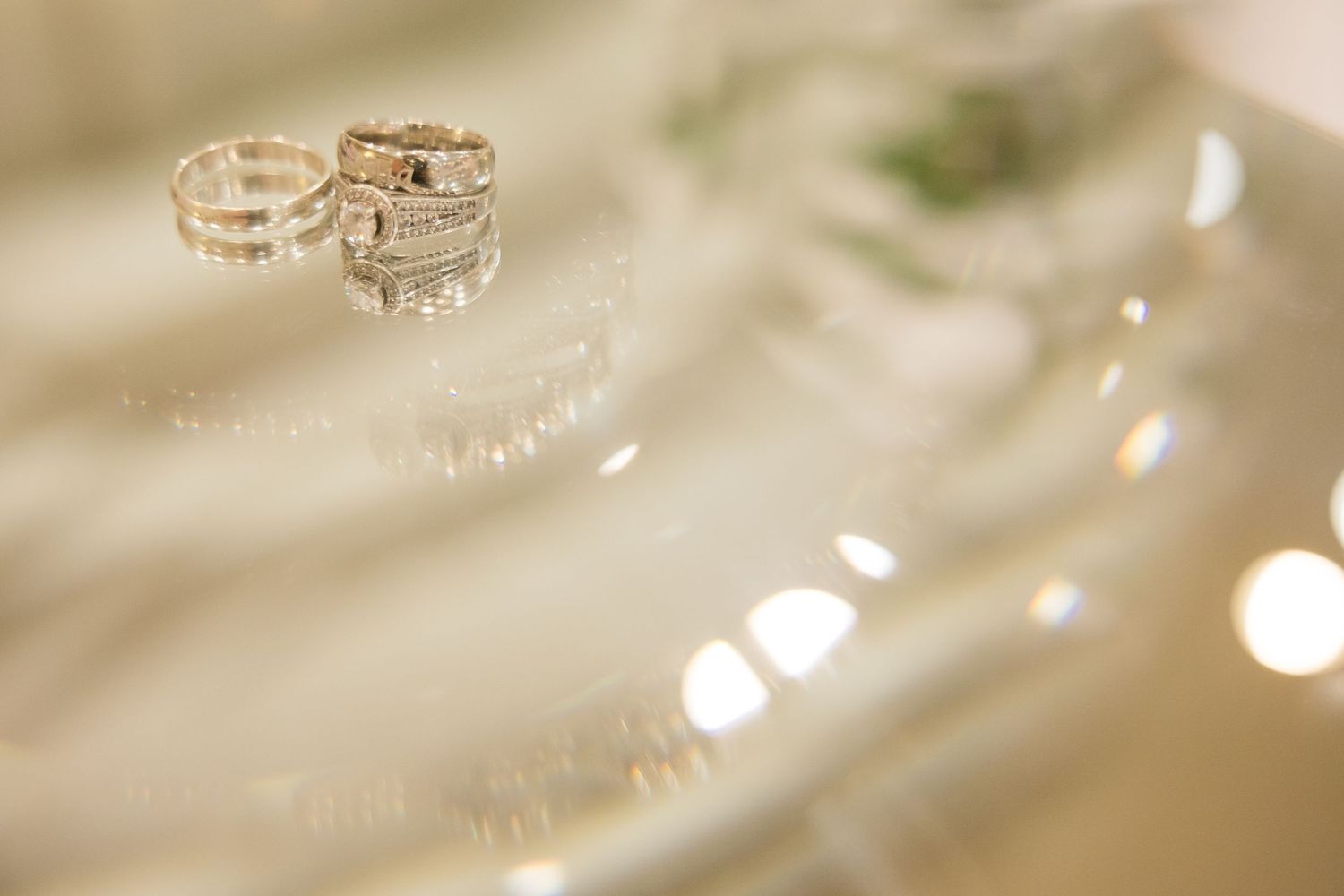 Close-up view of elegant wedding rings with diamond details on a soft white surface with bokeh light effects in background.