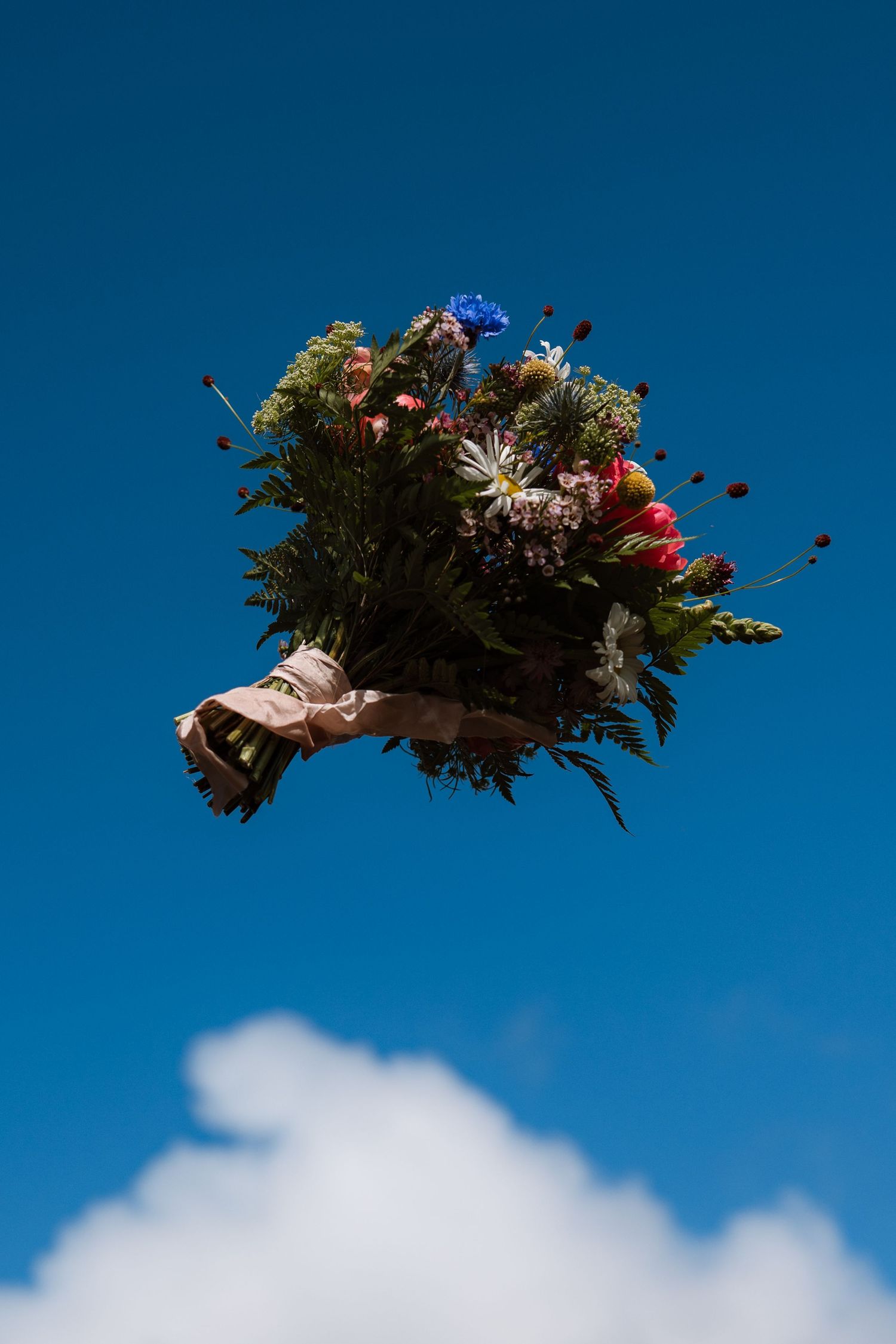 Wedding bouquet with colorful flowers floating against bright blue sky with white clouds.