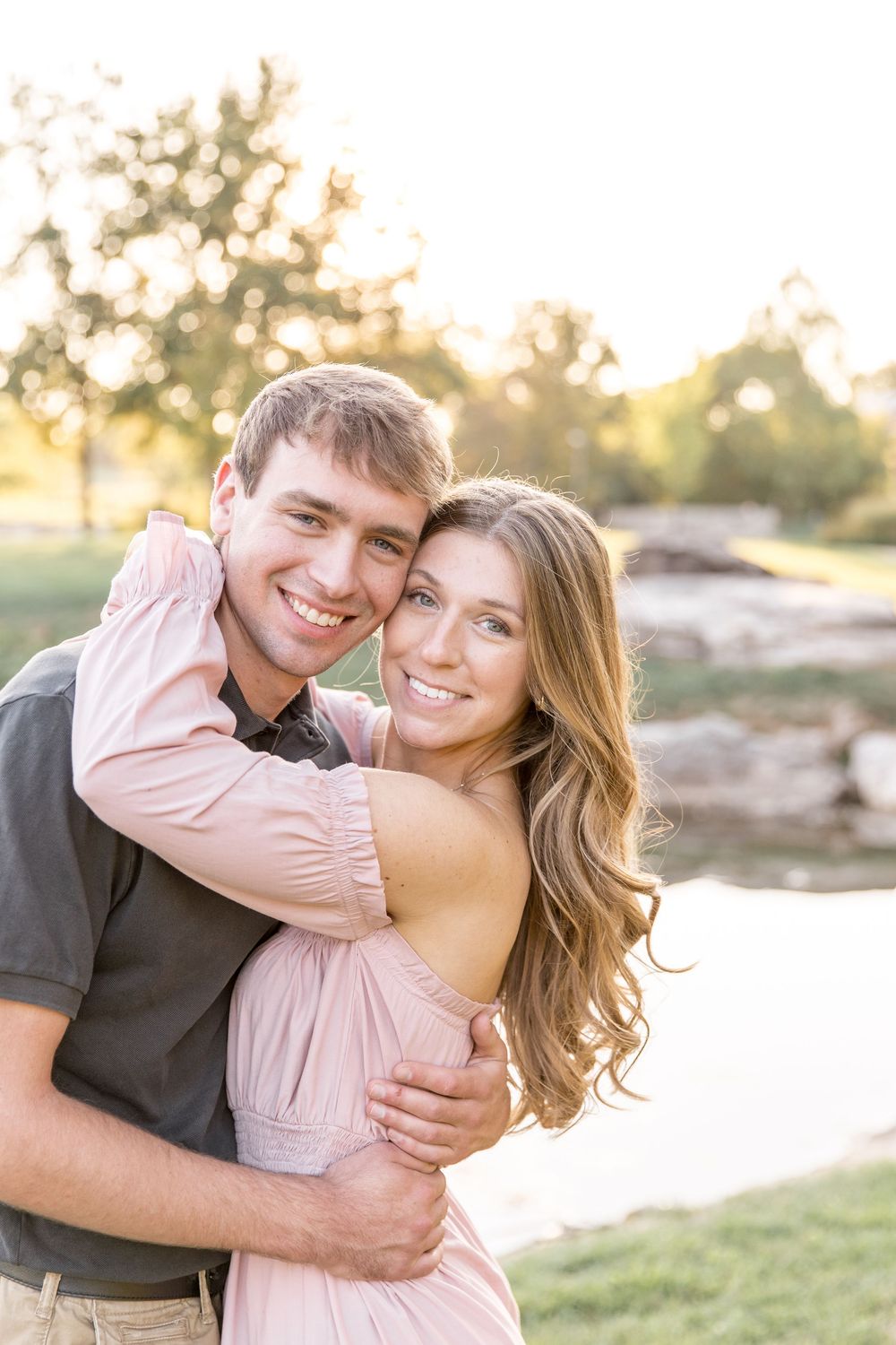 A couple embraces outdoors at sunset in a romantic photoshoot, with soft golden light and nature in the background.