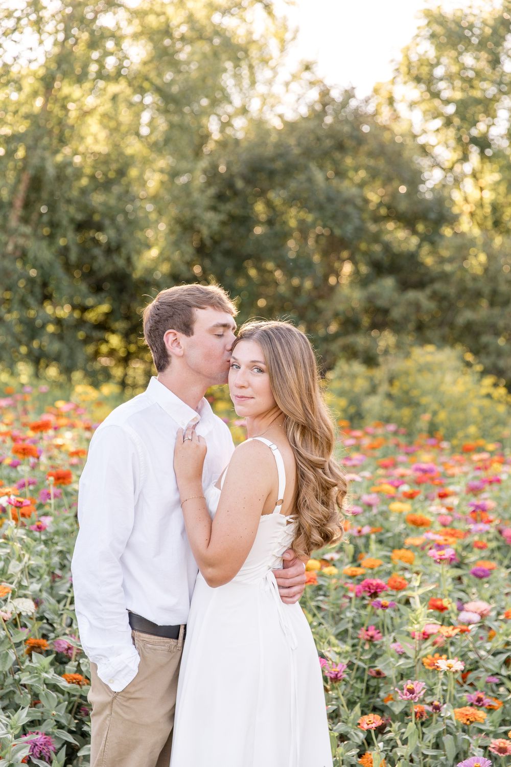 Romantic couple embracing in a colorful wildflower field at sunset during golden hour engagement photo session.