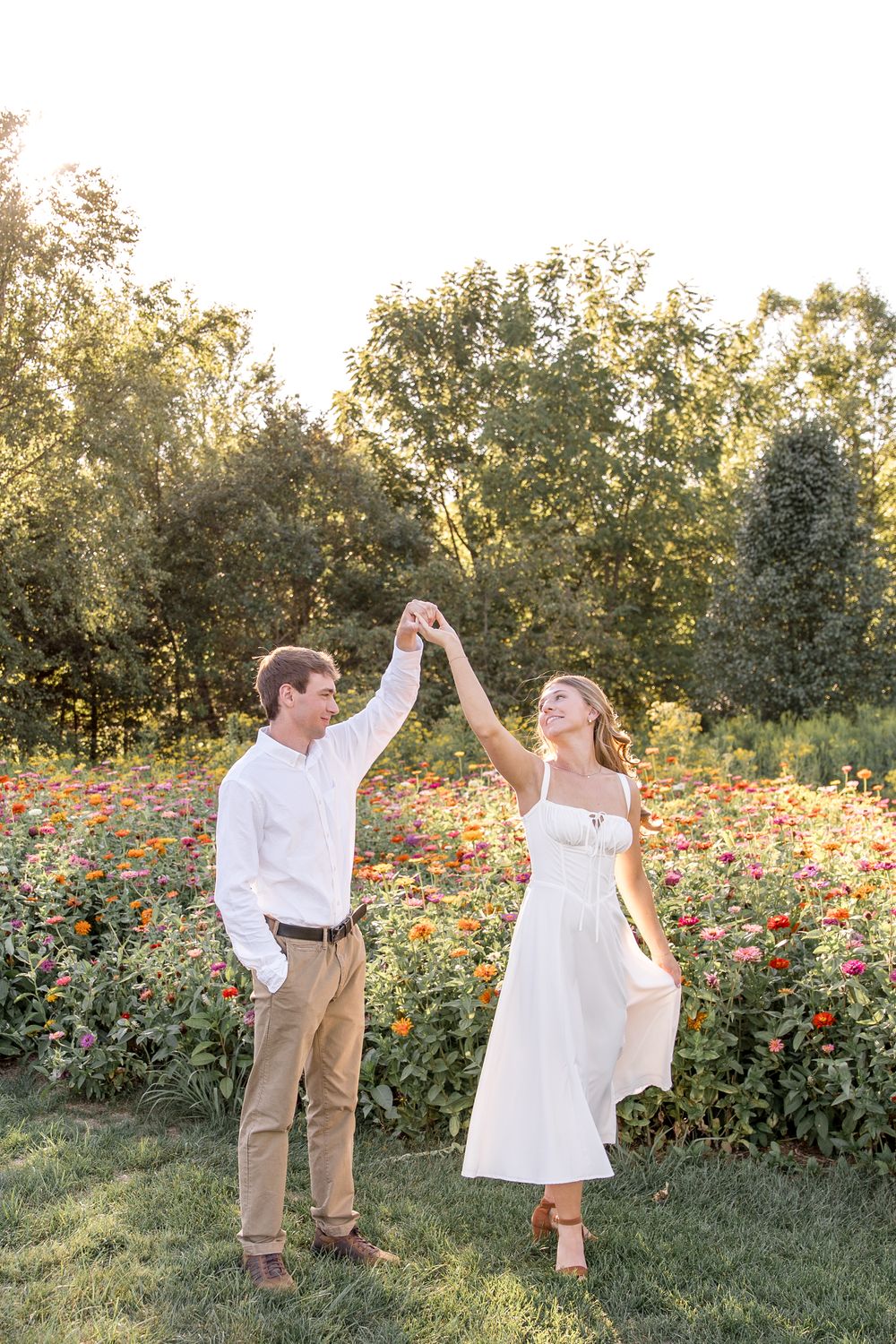 A couple dancing together in a garden filled with orange zinnias at golden hour.