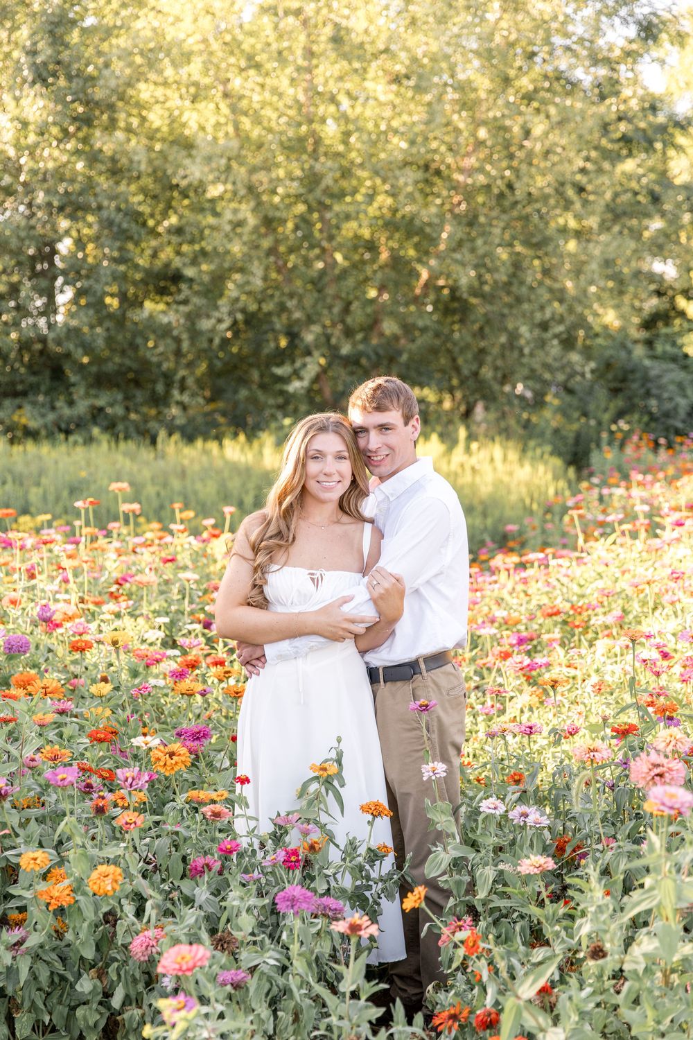 A couple embraces in a vibrant field of pink and orange zinnias during golden hour.