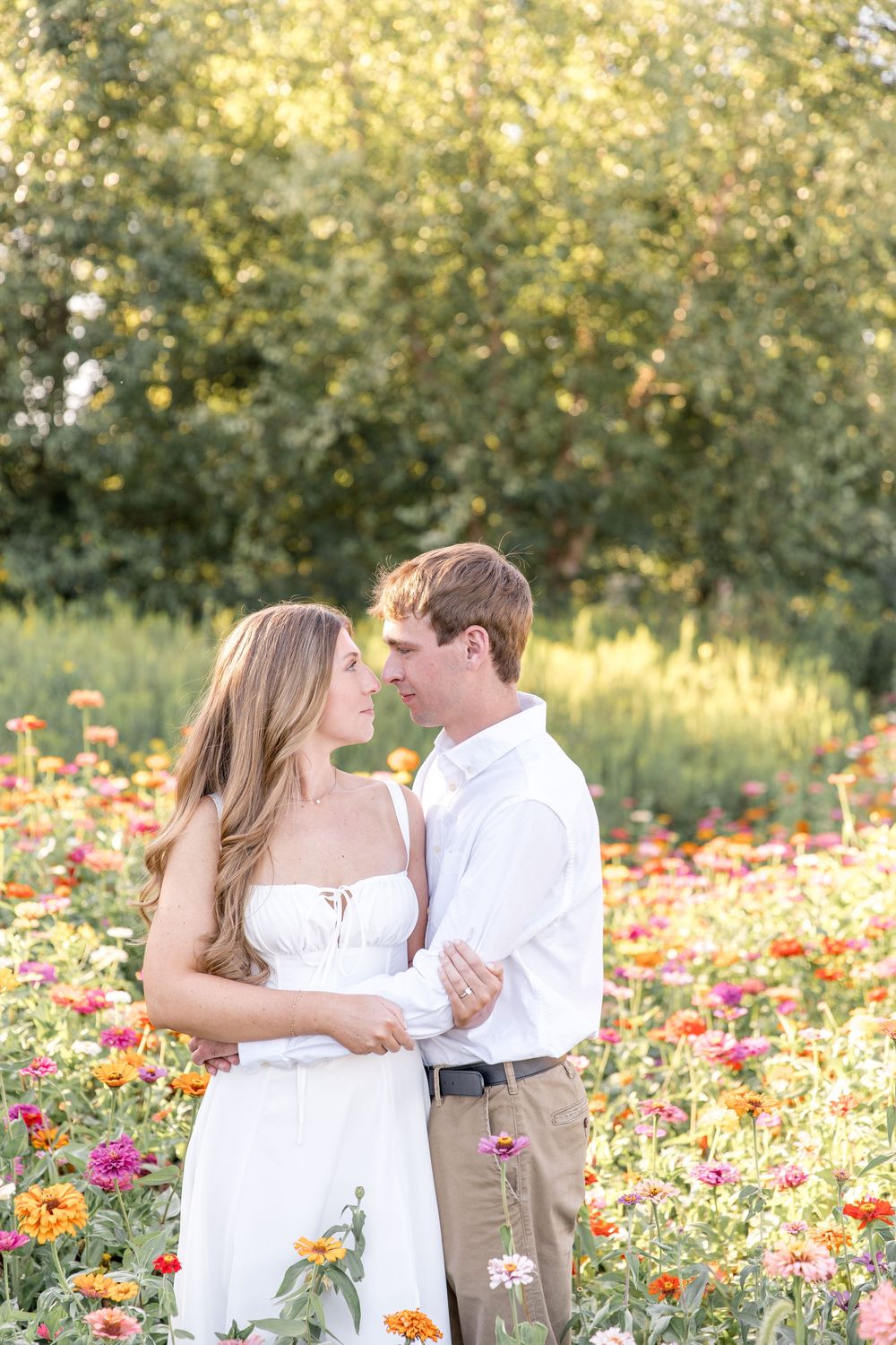 A romantic couple embraces in a beautiful wildflower field filled with vibrant orange and pink blooms at sunset.