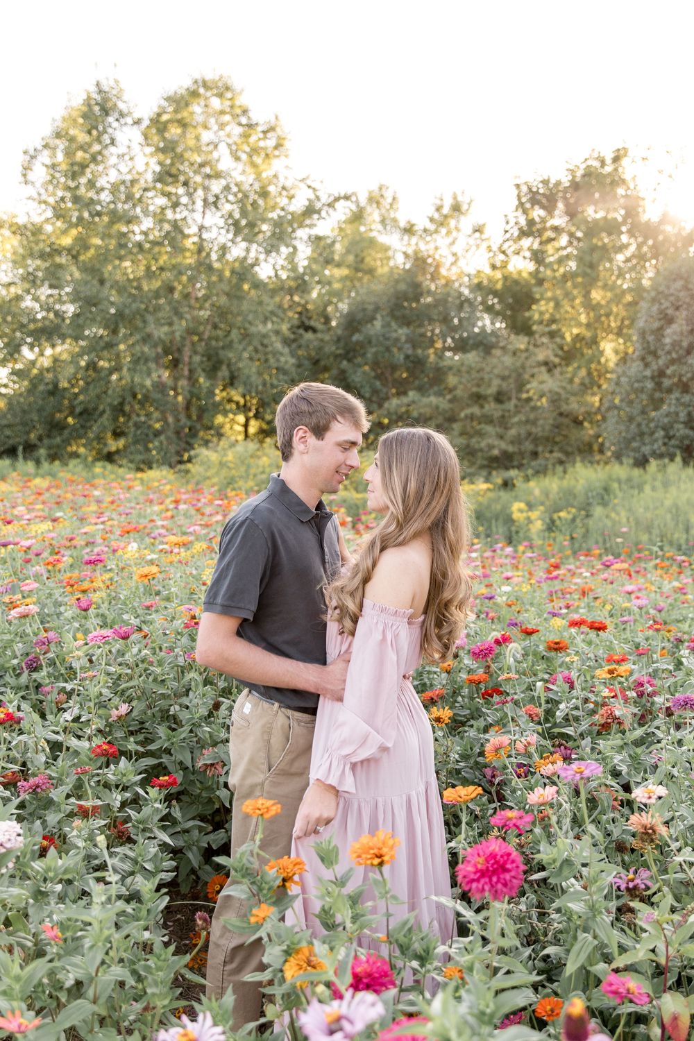 A couple shares a romantic moment in a vibrant garden filled with pink and orange zinnias at sunset.