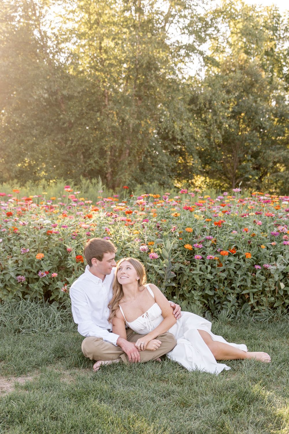 A couple sits in a meadow surrounded by colorful wildflowers during sunset, creating a romantic summer scene.
