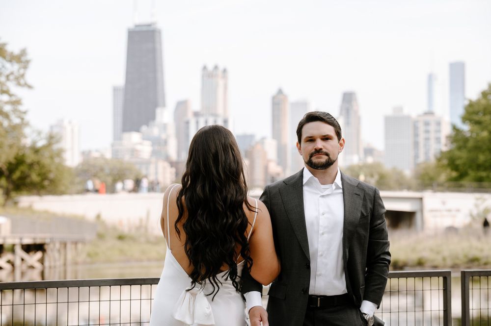 Two people stand on an outdoor viewing deck with the Chicago skyline rising behind them on a bright day.