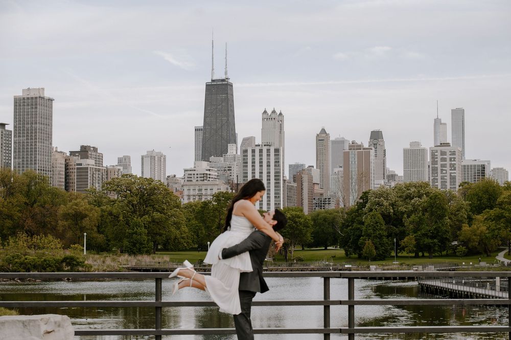 A couple embraces with Chicago skyline in background at Lincoln Park Zoo Nature Boardwalk during overcast day.