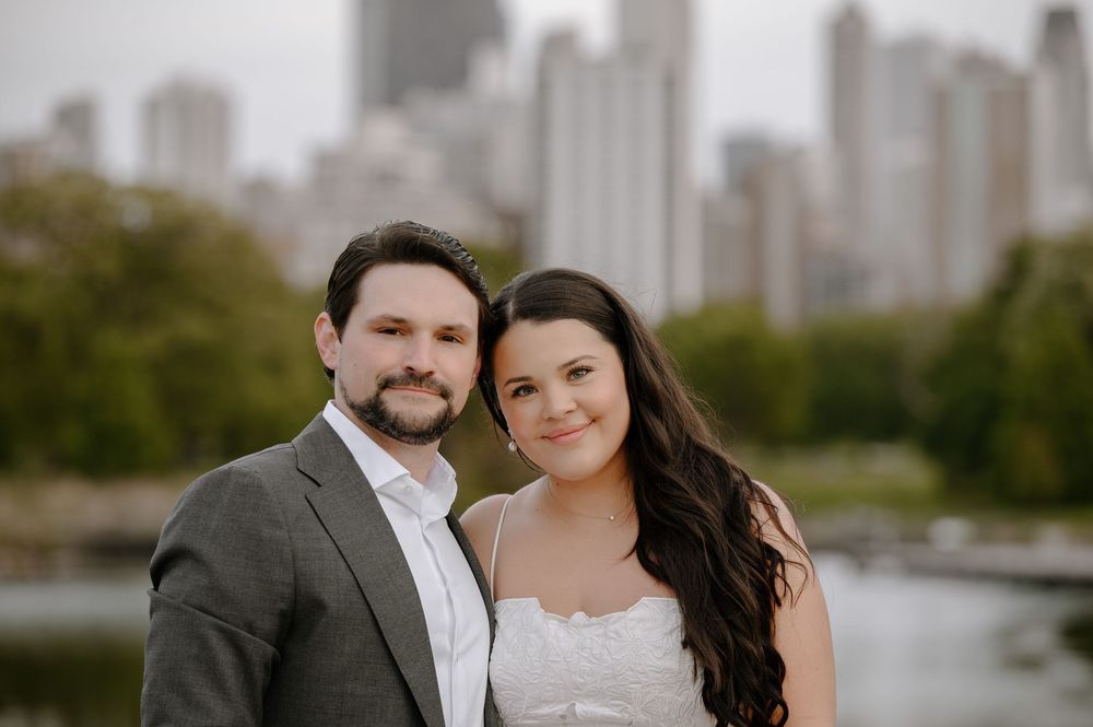 A happy couple poses together with downtown Chicago's skyline visible behind them on a cloudy day.