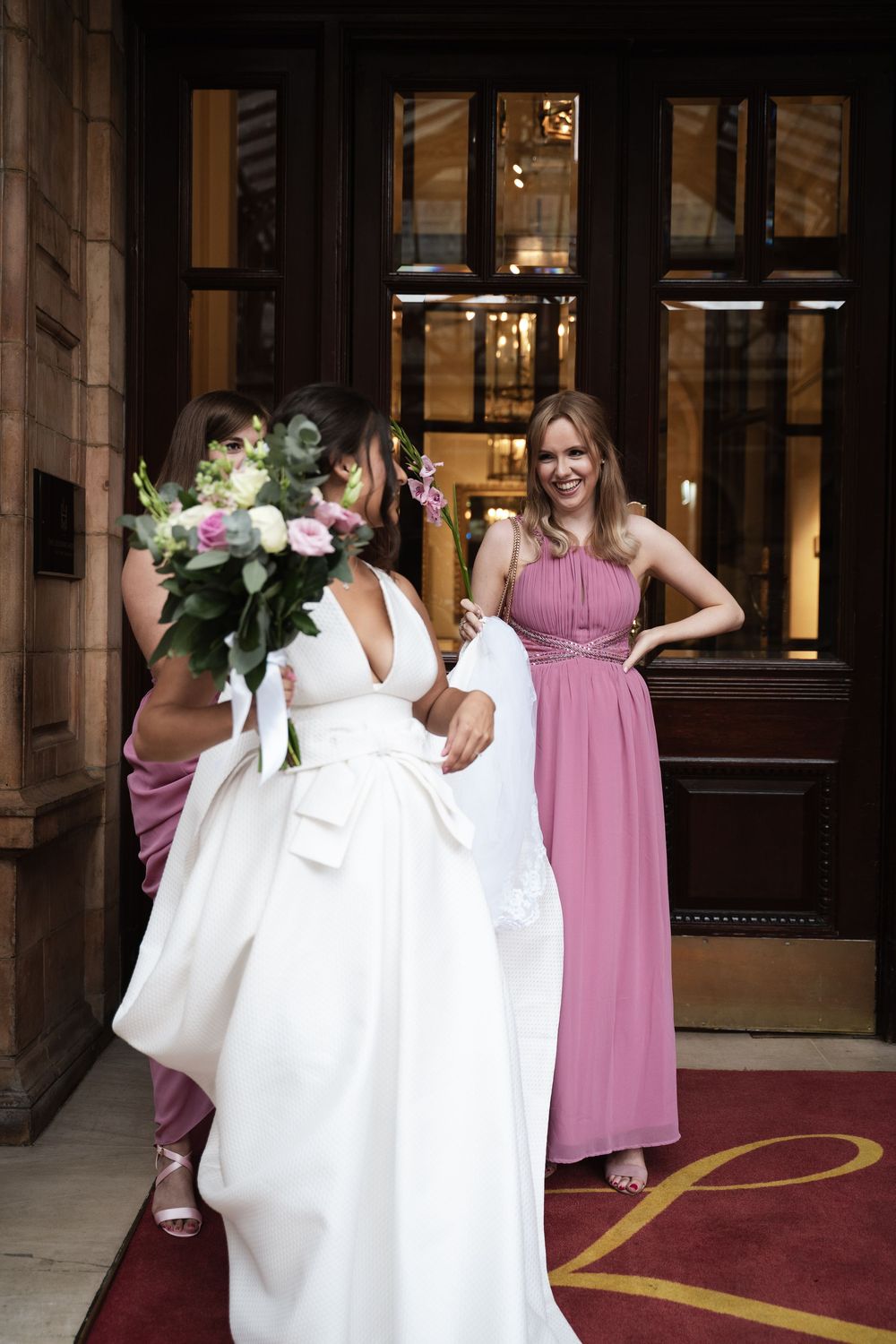 Wedding party with bridesmaids in pink dresses helping with the bride's gown.