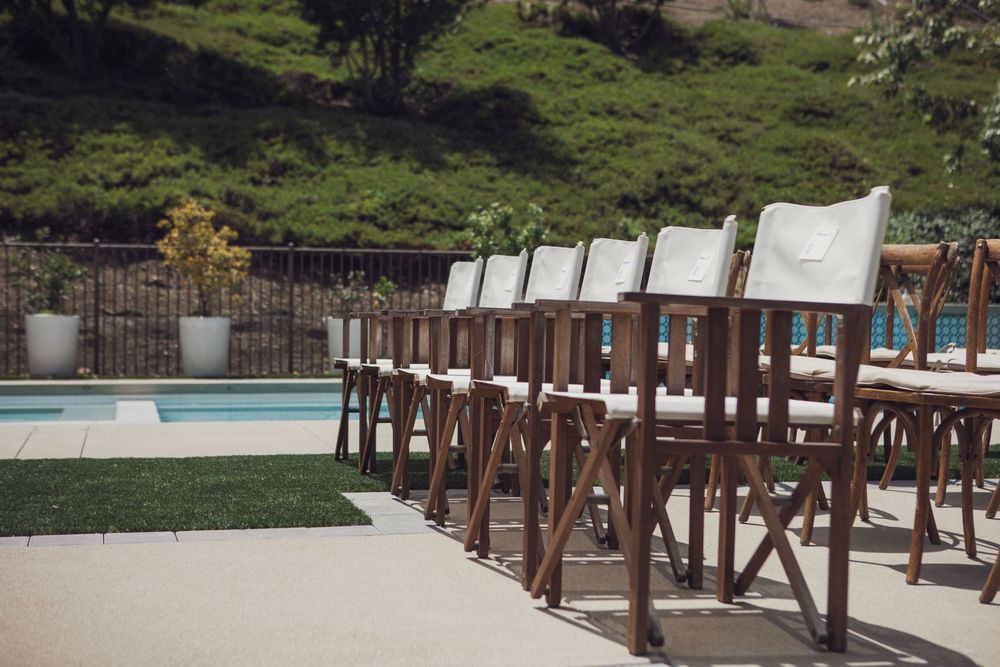 Curved wooden deck railing extends along an outdoor patio area with a pool and green lawn in the background.