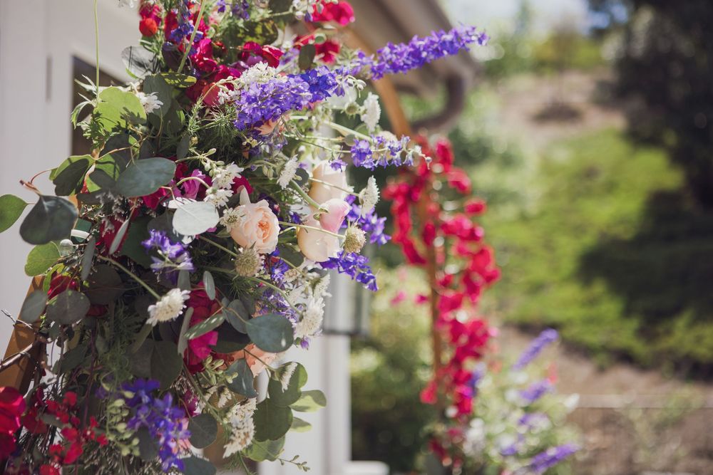 Vibrant floral arrangement with red and purple flowers cascading along white column in outdoor garden setting.