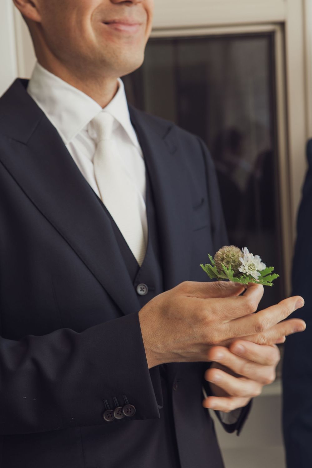 Close-up of person in navy suit with small succulent boutonniere pinned to lapel during formal occasion.