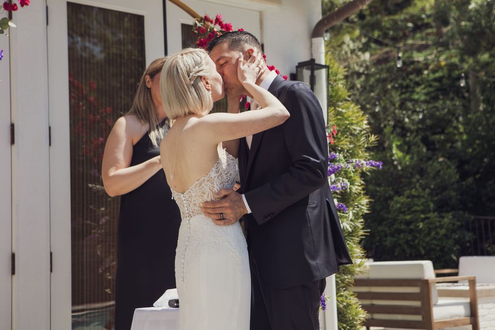 A couple shares a romantic moment during their outdoor wedding ceremony on a sunny day with natural decor.