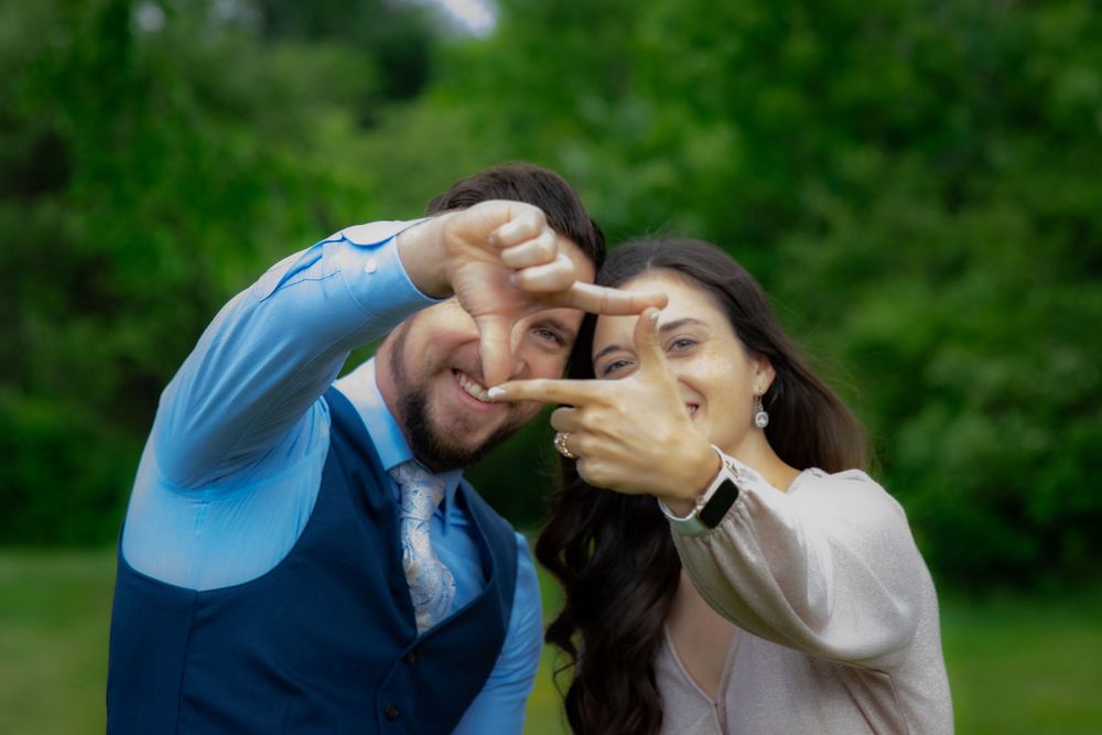 Two people making heart shapes with their hands while posing together outdoors in a green garden setting.