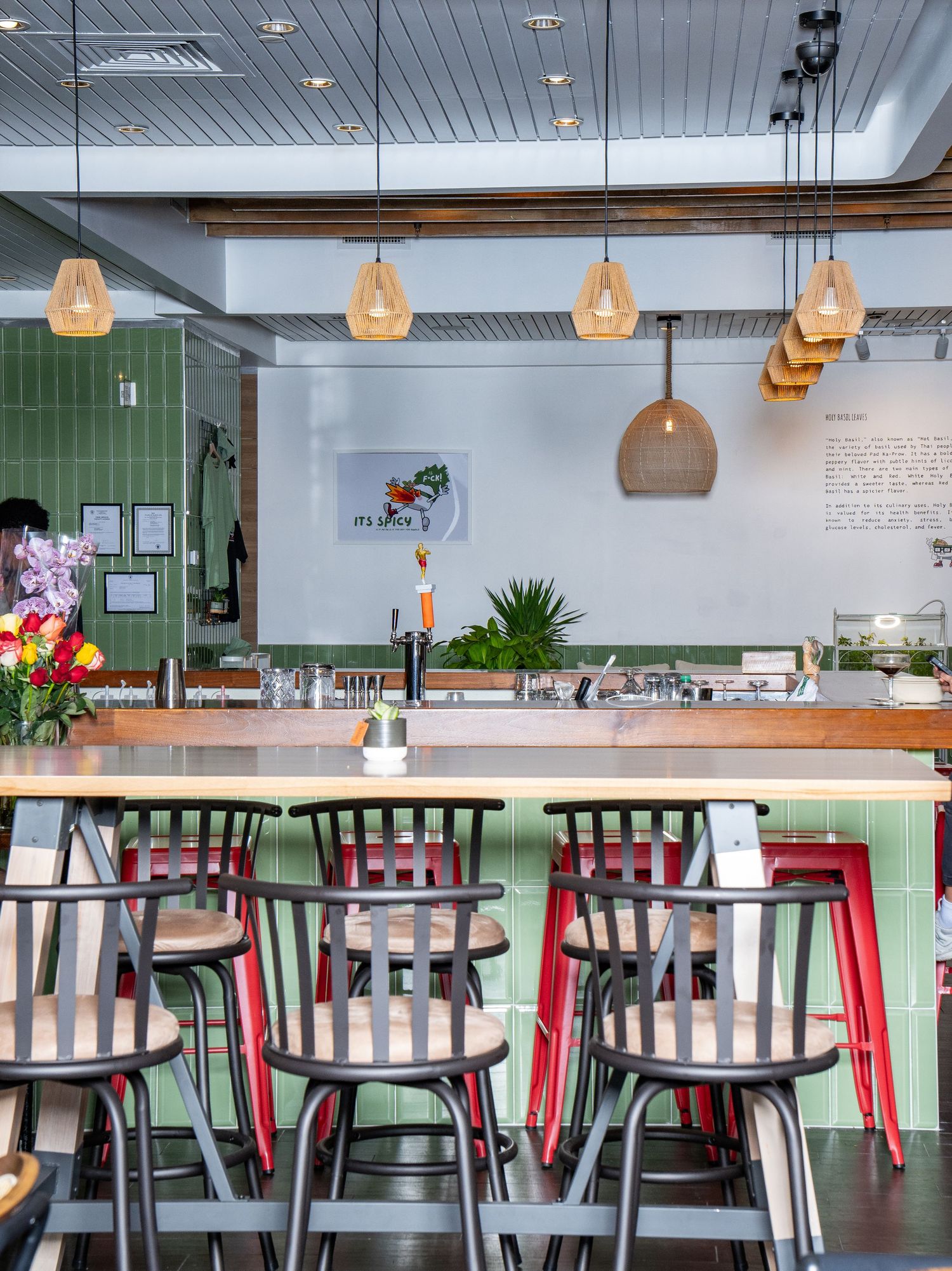 Modern cafe interior with wooden bar counter, green accents, pendant lighting and industrial-style chairs.