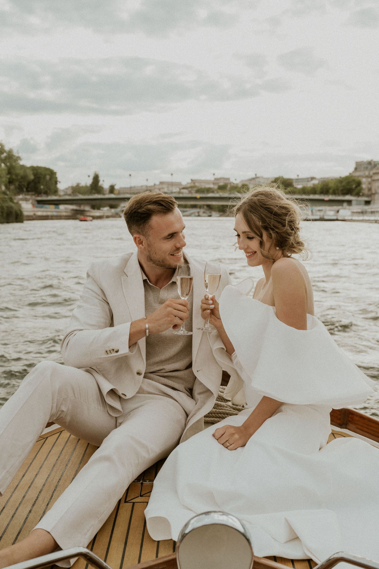 A romantic black and white photo of a couple on a boat by the Eiffel Tower in Paris with a bridge in the background.