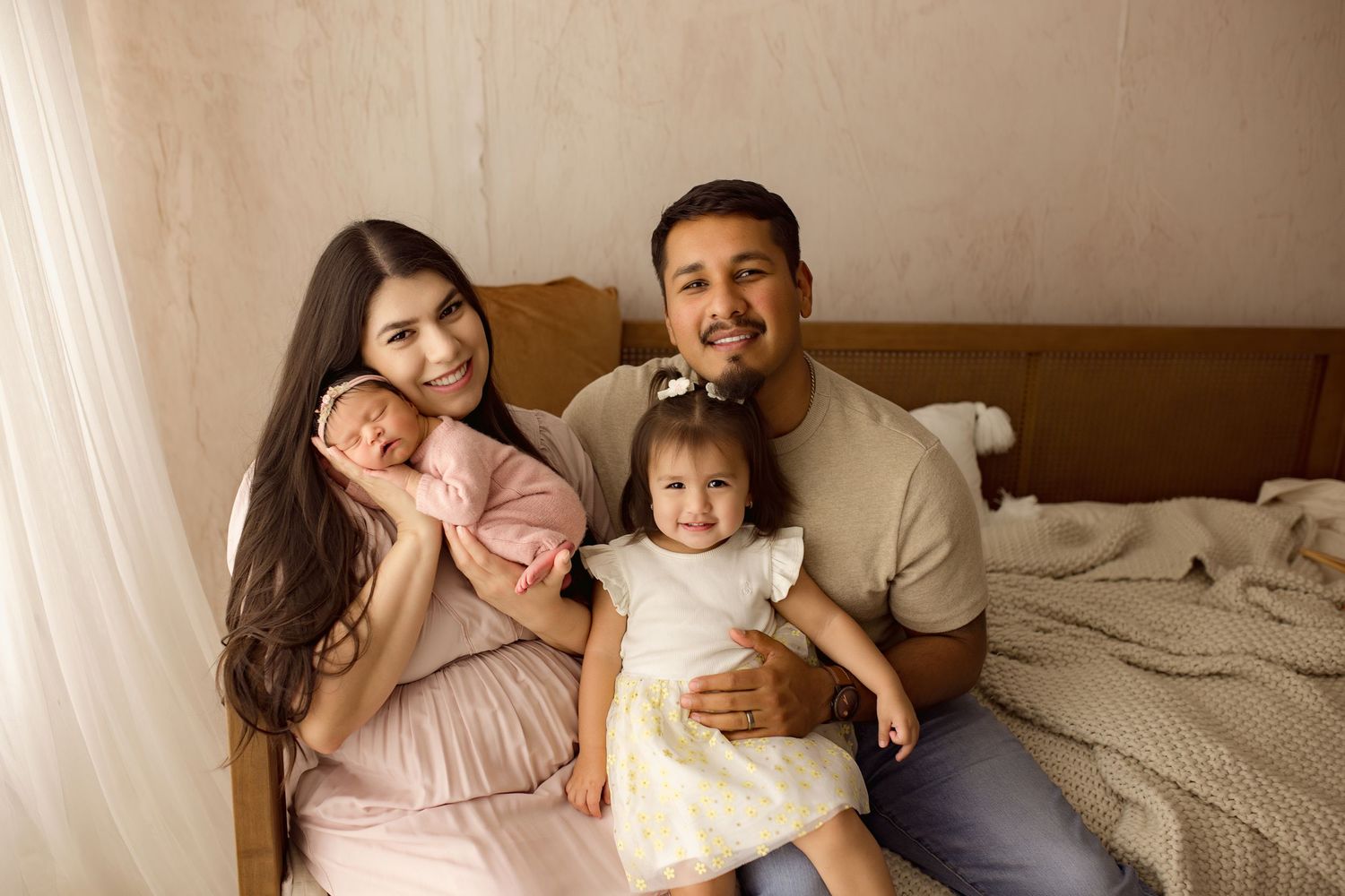 Happy family spending quality time together on bed with their children in a bright, cozy bedroom setting.
