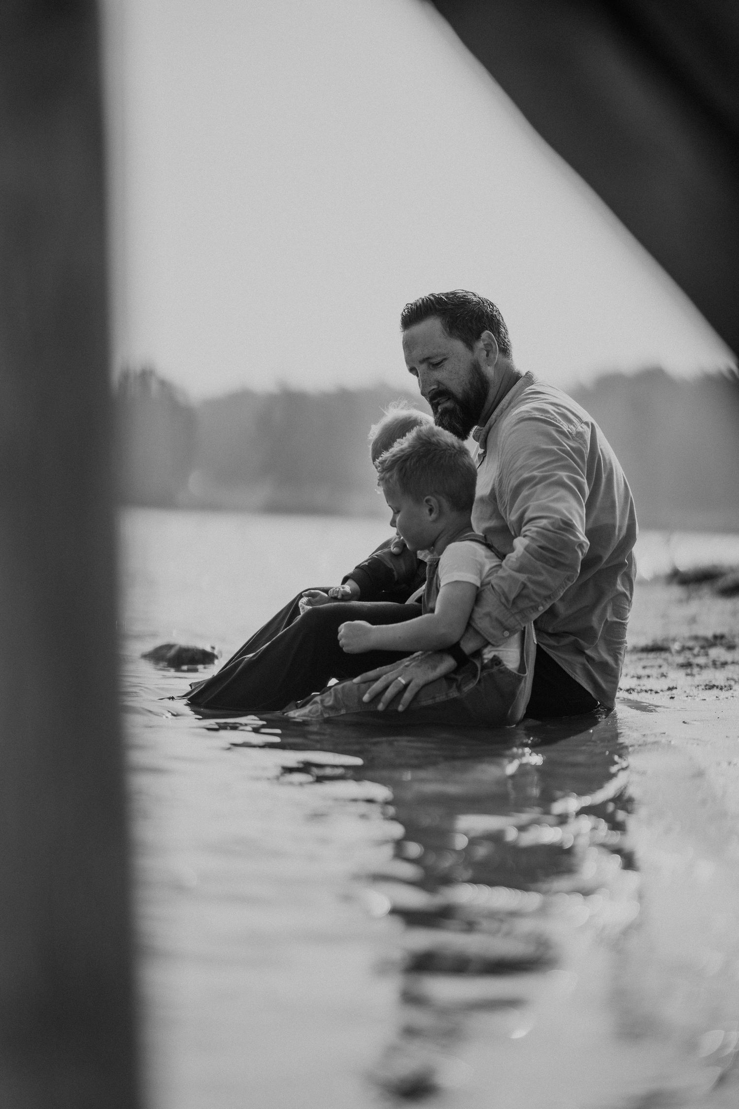 Een ouder en kind zitten aan de waterkant op een zwart-witfoto, een sereen en verbindend moment.