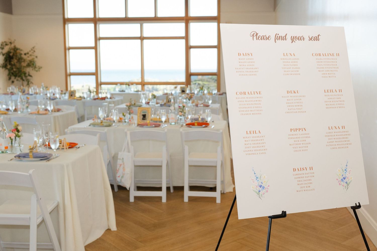 White wedding reception tables set with centerpieces and place settings next to a seating chart display on an easel.
