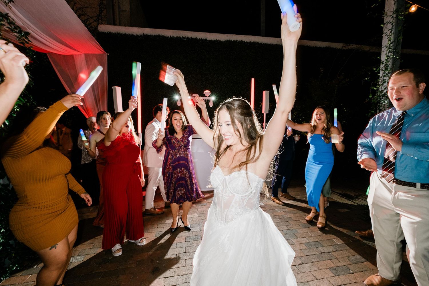 Wedding guests celebrate on dance floor during reception with arms raised in joyful celebration.