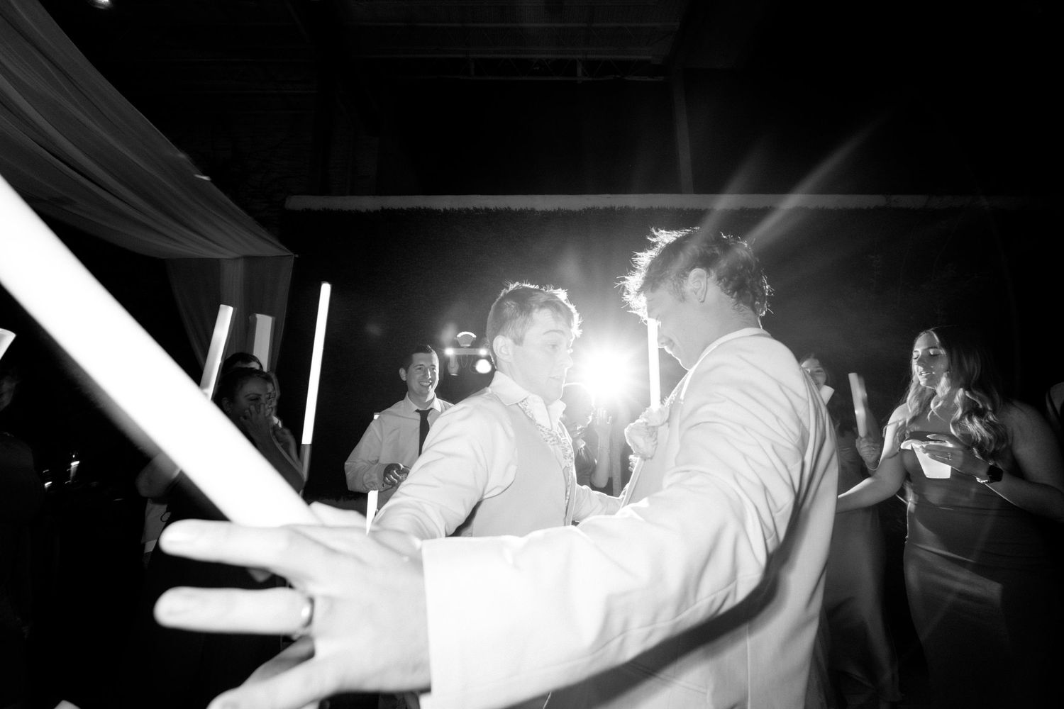 Two people share an intimate dance moment at a wedding reception with dramatic backlighting.