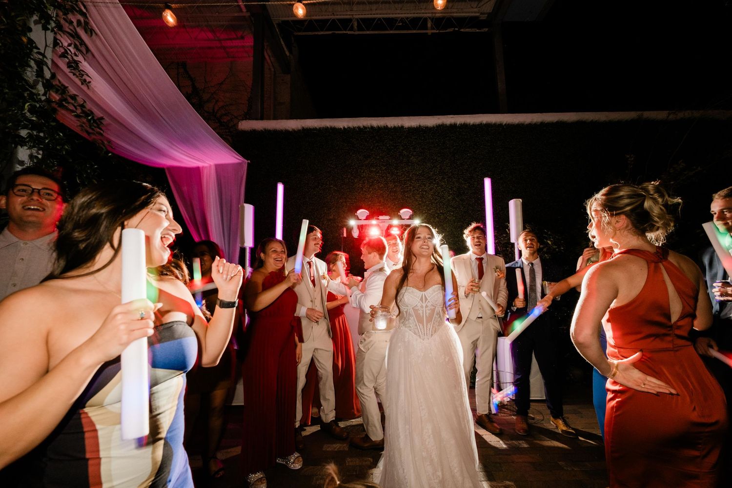 Wedding guests with sparklers surround a bride on the dance floor during an evening reception celebration.