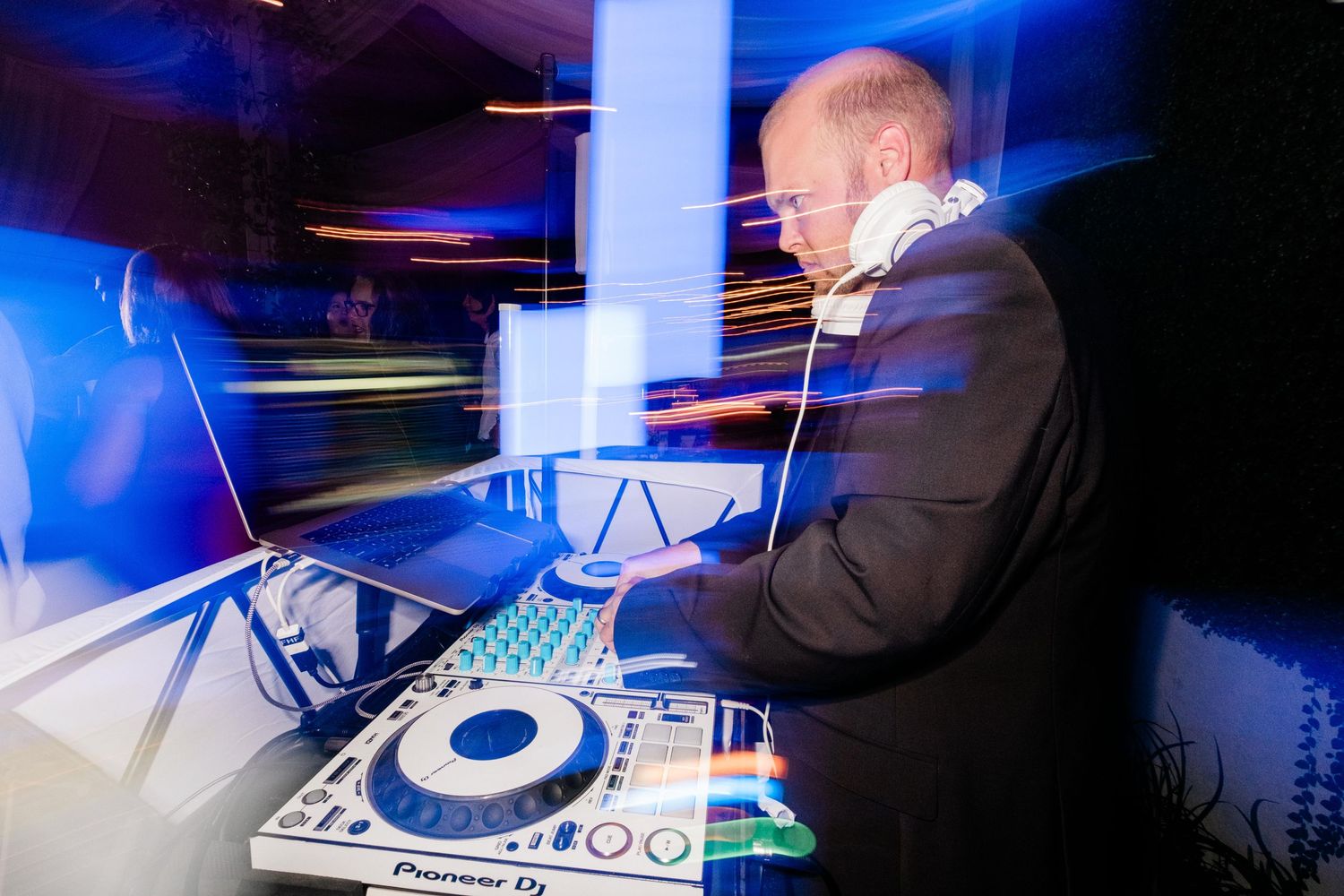 DJ performing at nightclub with blue lighting while mixing on professional DJ equipment and controller setup.