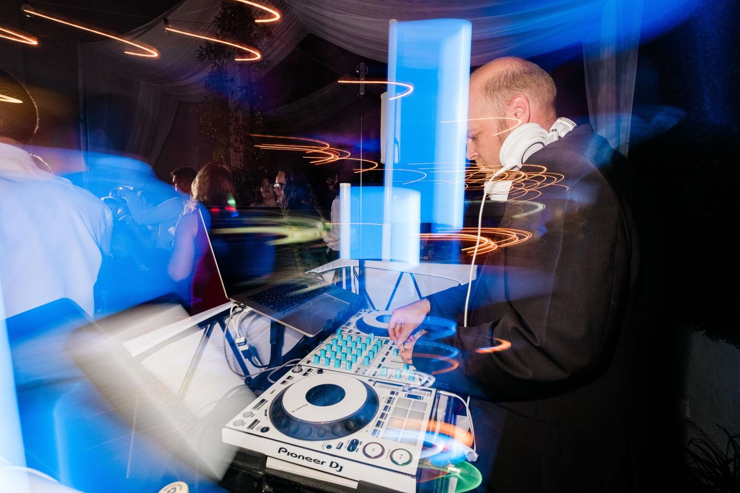 DJ mixing at a nightclub with blue lighting and motion blur effects creating streaks of light across the turntable setup.