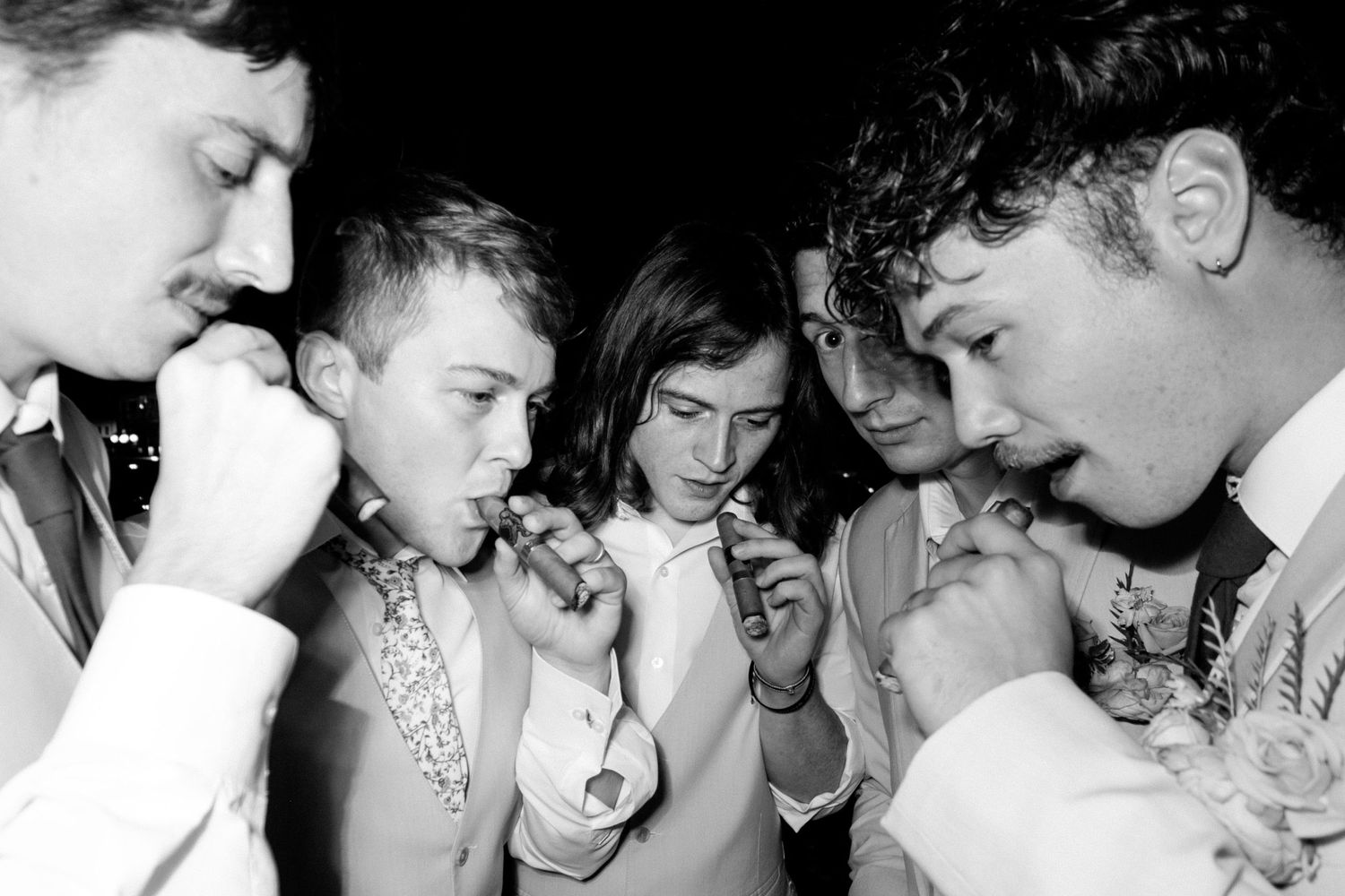 A black and white photograph of teenagers lighting cigarettes together in a close huddle.
