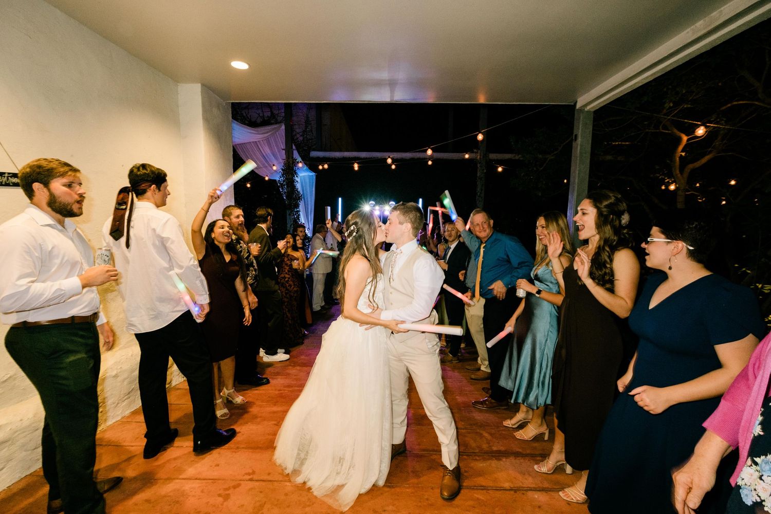 Wedding guests surround a couple dancing at a reception venue with blue lighting and indoor decor.