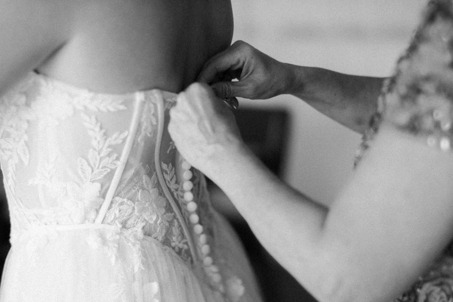 Close-up black and white photo showing delicate lace details being adjusted on a wedding dress.