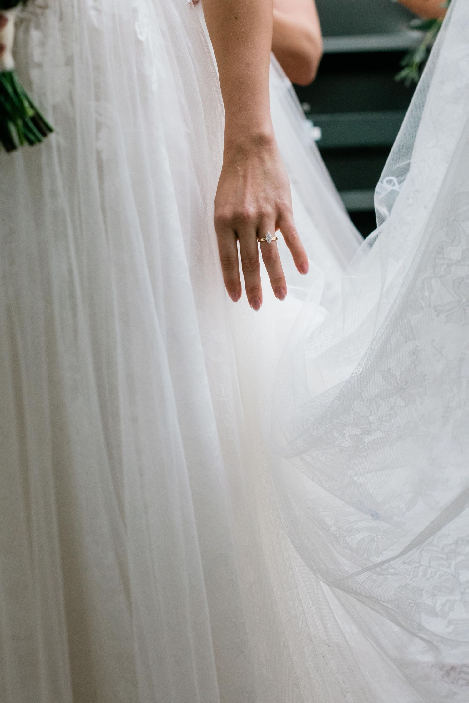 Close-up of a bride's hand showing wedding ring against white dress fabric.