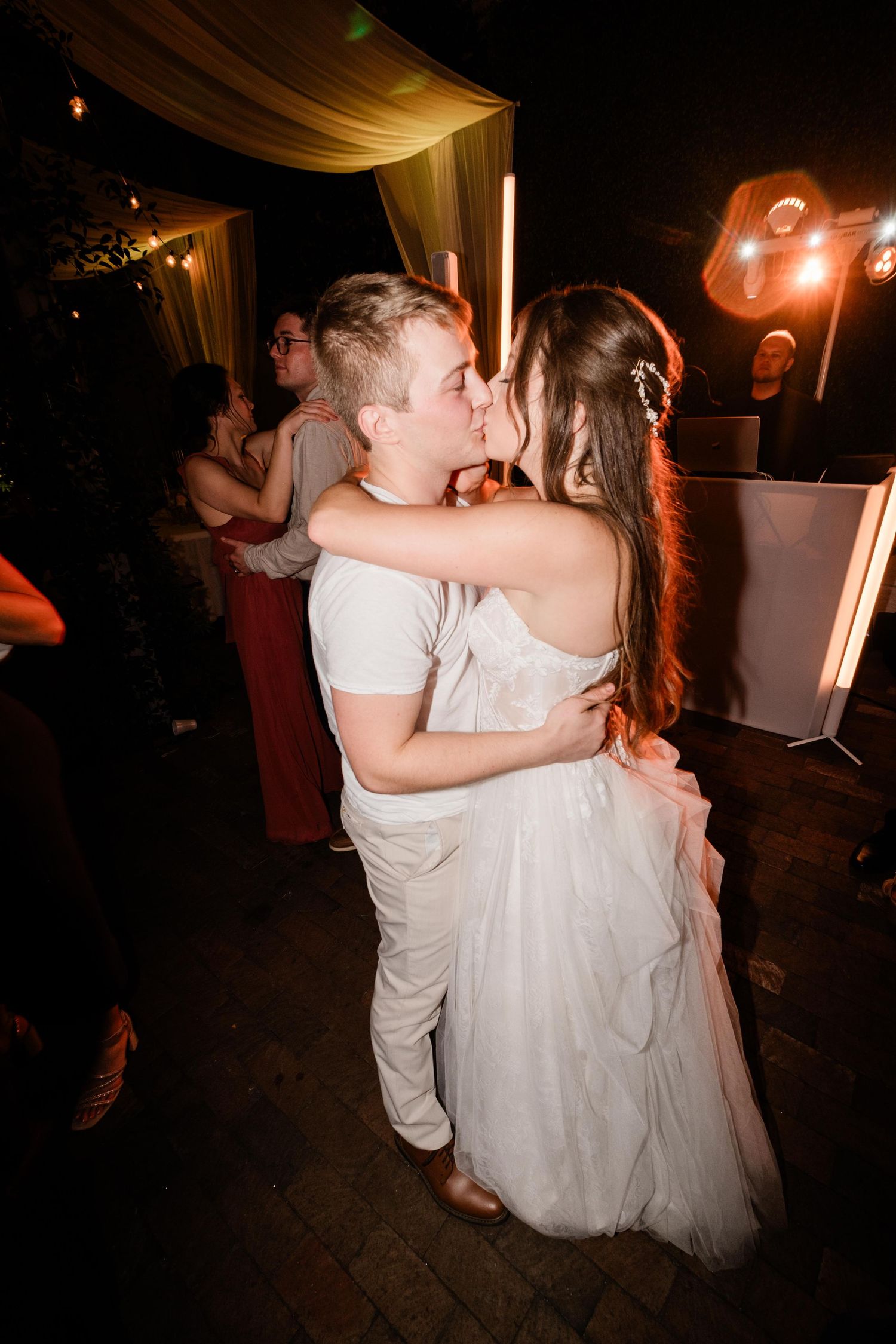 A couple shares their first dance at a wedding reception under warm lighting and draped fabric.