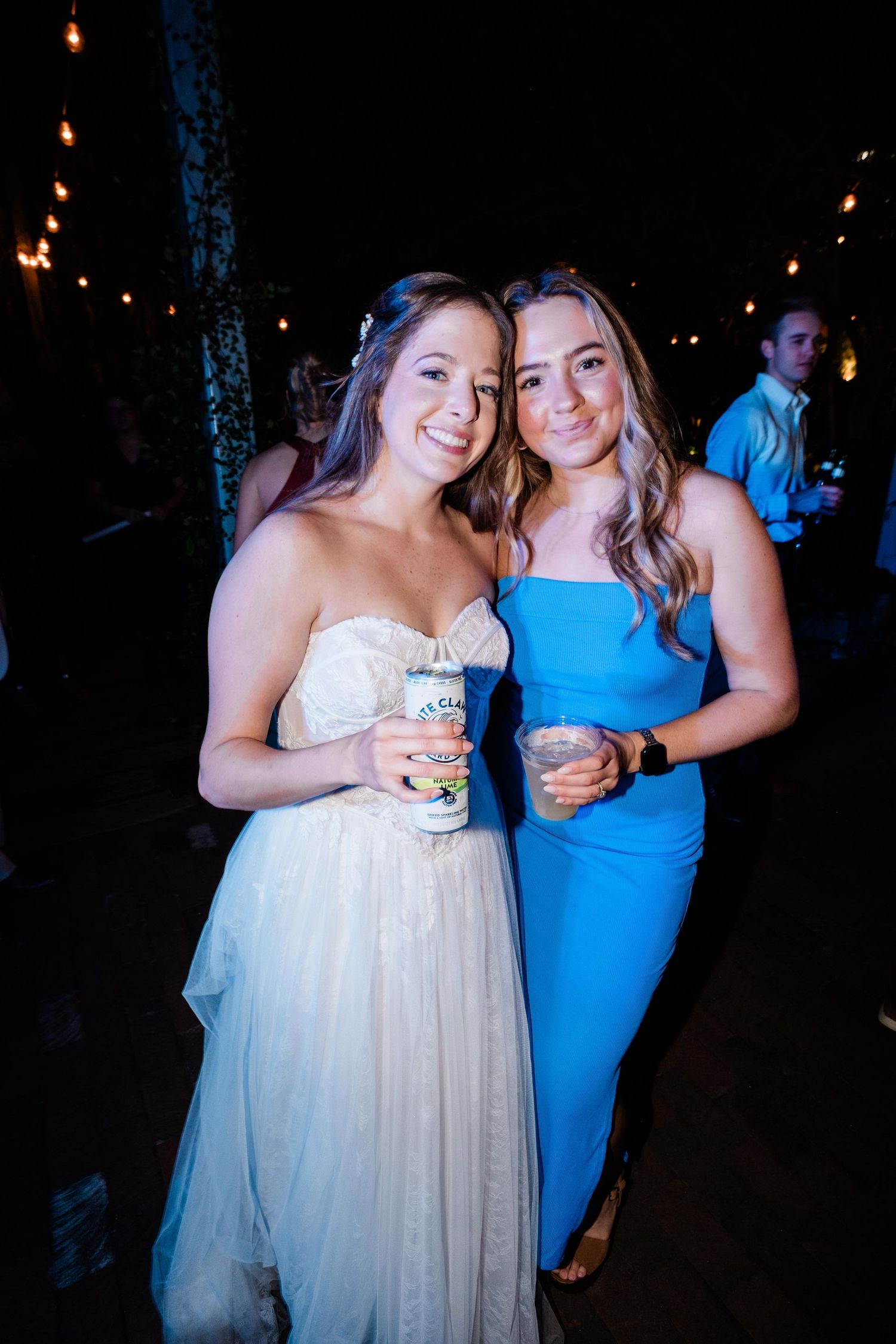 Two wedding attendees pose at an evening reception with string lights in the background.