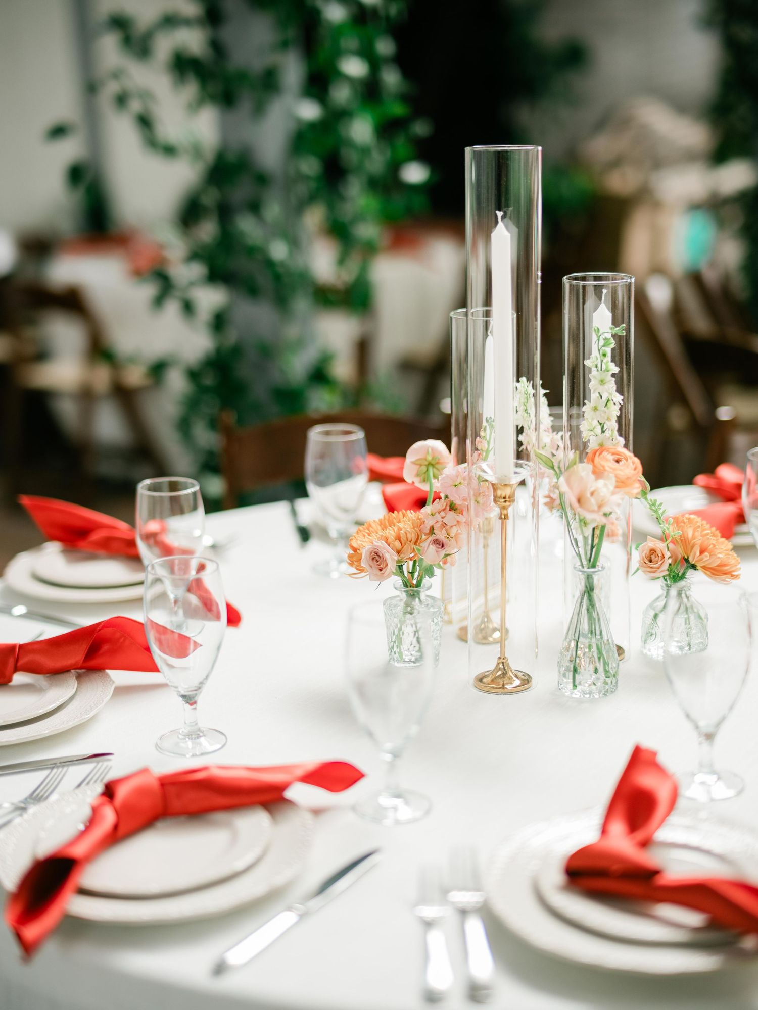 Elegant wedding table setting with white linens, coral napkins, tall candle centerpieces and delicate floral arrangements.