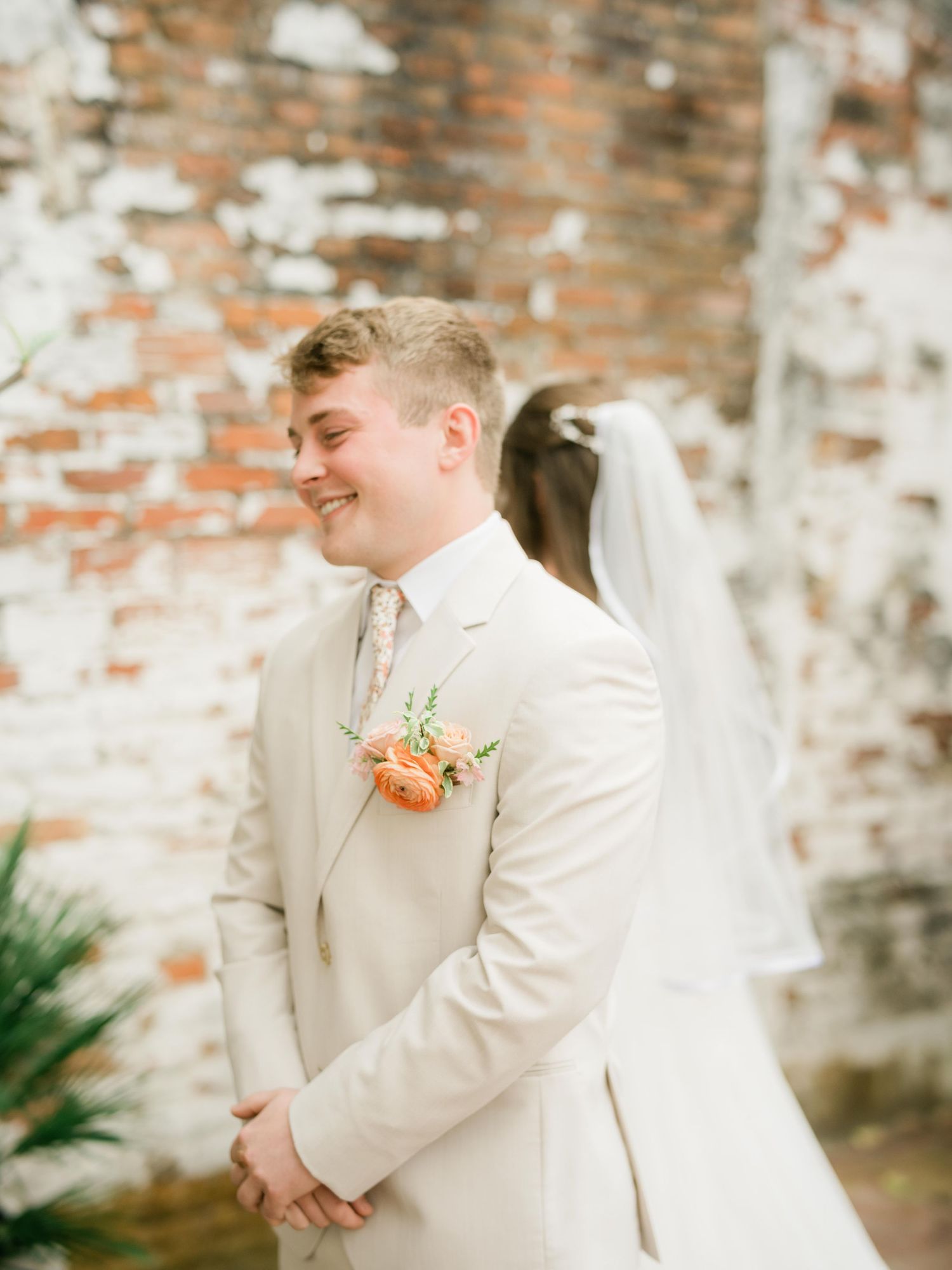 A joyful moment during a wedding ceremony with someone in a cream-colored suit and peach boutonniere.
