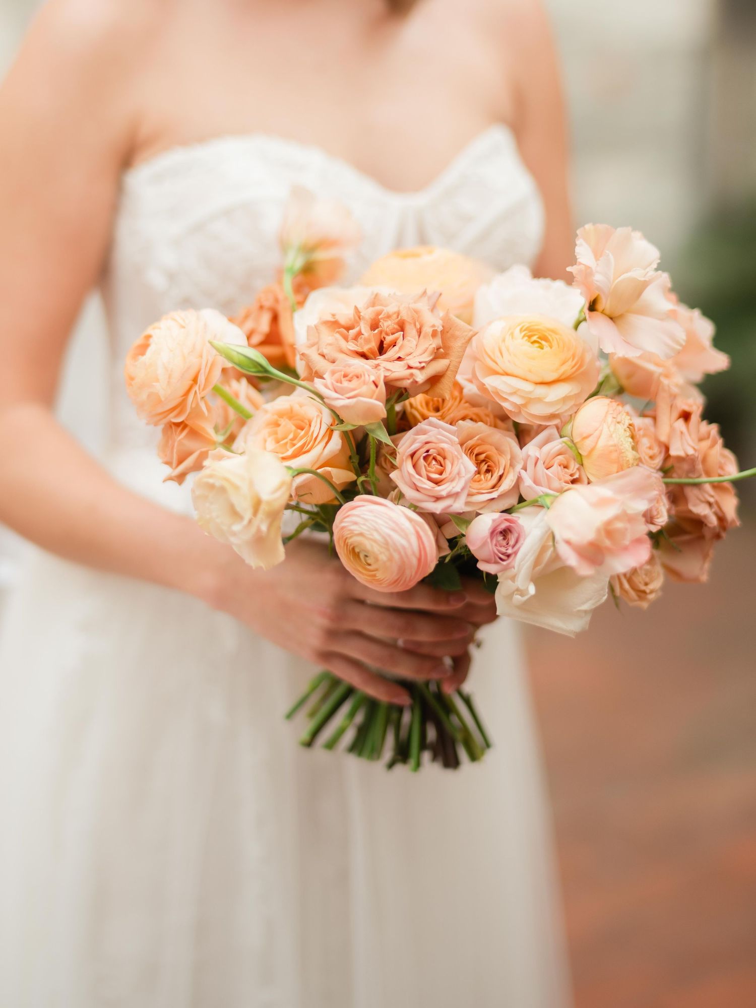 Delicate peach and blush garden roses arranged in a romantic bridal bouquet against a white dress.