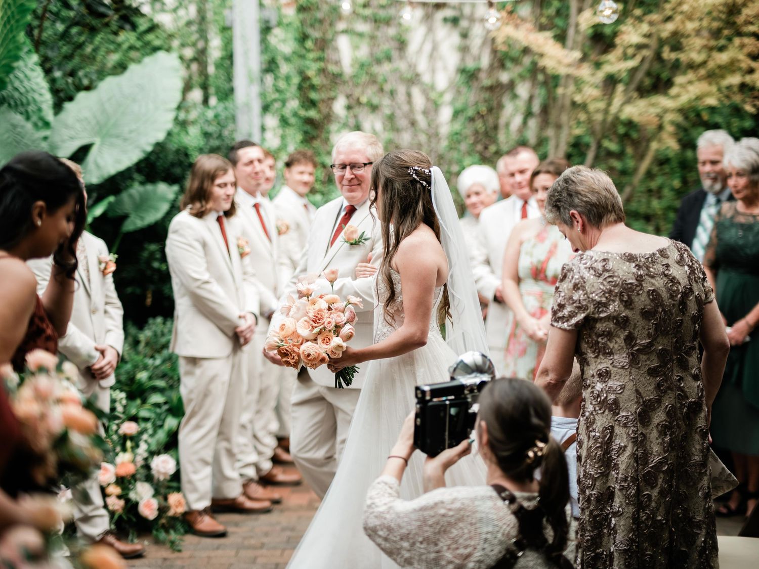 Wedding ceremony in a lush garden setting with guests in white attire watching the couple.