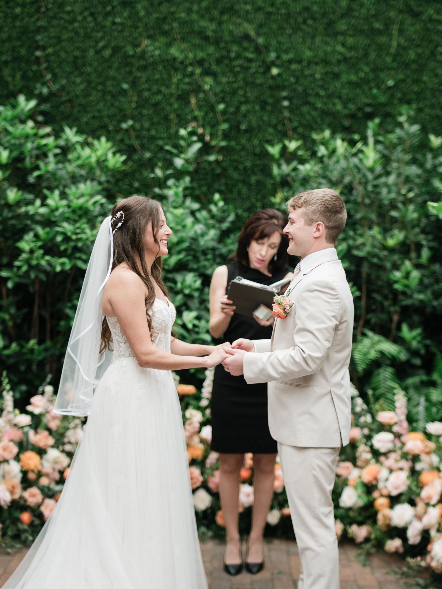 An outdoor garden wedding ceremony with a couple exchanging vows in front of floral arrangements and greenery.